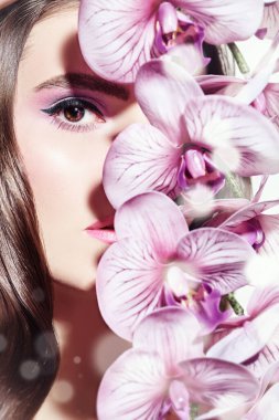 Orkide çiçekleri olan güzel romantik bir kadının yakın plan portresi. Makyaj ve makyaj malzemeleri. Güzellik ve sağlık hizmetleri.