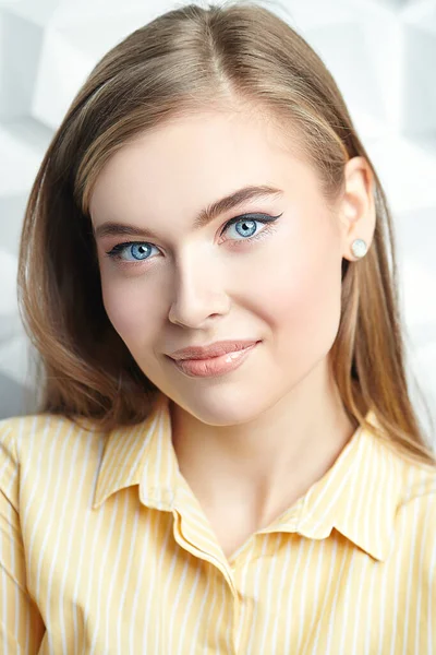 Beautiful young woman in a blouse and with natural make-up looks at the camera and smiles. Business lady. Studio portrait on a white background.