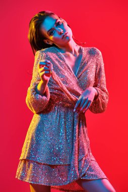 Makyaj ve makyaj malzemeleri. Renkli kırmızı, mavi ve sarı ışıkta elinde şampanya bardağıyla poz veren altın makyajlı genç bir kadının portresi. Parti biçimi. 