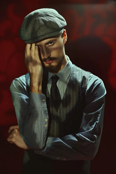 Portrait of a handsome man in elegant classical suit and a cap standing in the dark with shadows falling on it. Retro style. Criminal world, detective.