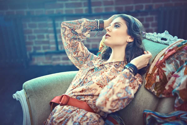 Bohemian style. Fashion shot of a beautiful young woman in boho style dress and jewelry posing in a vintage armchair.
