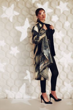 Moda fotoğrafı. Güzel, modaya uygun bir model, yıldızlı beyaz bir arka planda şık kıyafetler giyiyor. Stüdyo resmi. 