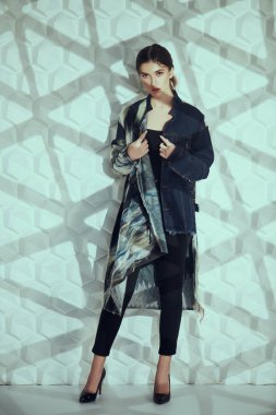 Moda fotoğrafı. Geometrik gölgeli beyaz bir arka planda şık kıyafetlerle poz veren güzel modaya uygun bir model. Stüdyo resmi. 