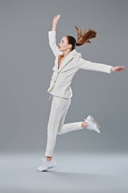 Moda fotoğrafı. Gri arka planda koşan beyaz takım elbiseli güzel bir genç kadının portresi. Mavi akuamarin göz oklarıyla modaya uygun makyaj. Makyaj ve kozmetik. 