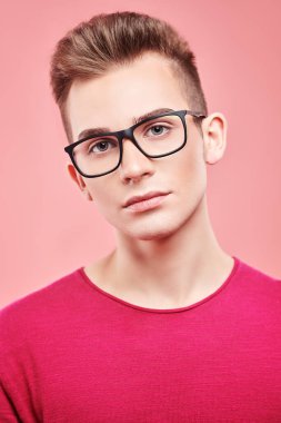 Gençlik modası. Modern kıyafetler ve gözlüklerle pembe arka planda poz veren zarif genç adam..