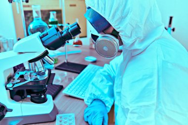 COVID-19 ve ilaç. Bir doktor, mikrobiyolog, koruyucu kıyafetli bir bilim adamı laboratuvarda mikroskop kullanarak koronavirüsü inceliyor..