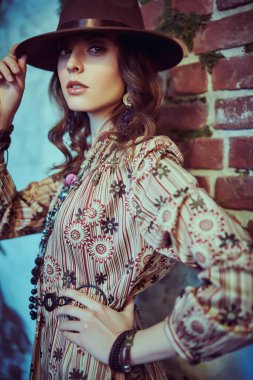 Boho tarzı elbise ve aksesuar giymiş muhteşem bir genç kadının portresi harabe duvarların arka planına poz veriyor, yosunla kaplanmış. Bohem, modern hippi tarzı..