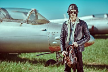 Kask ve deri ceket giyen yakışıklı pilot savaş uçağının yanında duruyor. Askeri uçak..