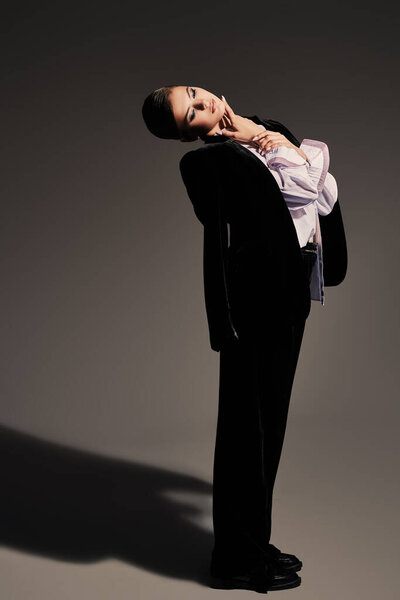 Fashion concept. Full length portrait of a gorgeous graceful young woman model posing in black velvet suit and white shirt on a gray background. 