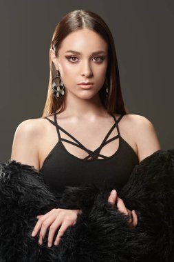 Stüdyoda siyah kıyafetler ve gri arka planda siyah kürklü poz veren çekici bir manken. Güzellik, moda.