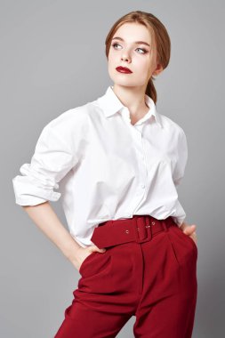 Güzellik, moda portresi. Zarif bir iş tarzı. Beyaz bluzlu ve kırmızı pantolonlu güzel sarışın bir kadının portresi stüdyoda gri arka planda poz veriyor..