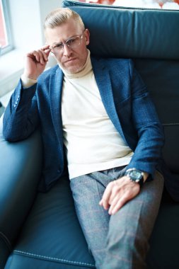 Zarif takım elbiseli ve deri koltukta rahatça oturan orta yaşlı yakışıklı bir işadamının portresi. Başarı ve liderlik.