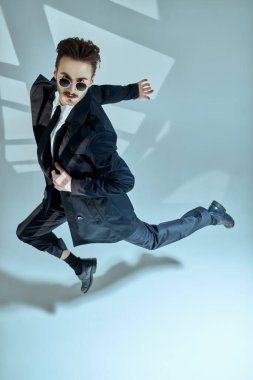 Modern şehir yaşam tarzı. Palto ve güneş gözlüklü şık genç adam sarı sanayi duvarının oradaki bir sokakta koşuyor. Erkek modası. 