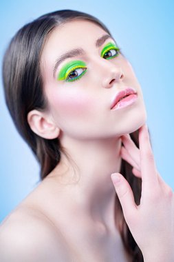 Makyaj ve makyaj malzemeleri. Mavi arka planda canlı renkli makyajlı güzel bir kızın yakın plan portresi..