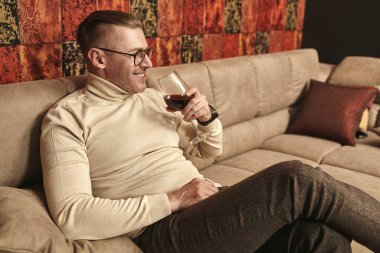 Saygıdeğer orta yaşlı bir adamın portresi günlük kıyafetler ve gözlüklerle lüks bir dairede kırmızı şarap içen. Başarı ve zengin yaşam tarzı.