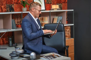 Takım elbiseli ve gözlüklü saygıdeğer orta yaşlı işadamı modern bir ofiste çalışıyor. Başarılı yönetici kavramı.