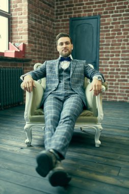 Yakışıklı beyefendi, çatı katındaki eski bir koltukta rahatça oturuyor. Tam boy portre.
