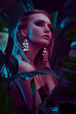 Islak saçlı güzel ateşli kadın tropikal bitkilerin arasında duruyor. Güzellik, moda ve kozmetik konsepti. Tropikal ülkelerde tatil.