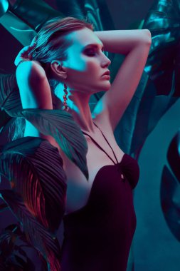 Islak saçlı güzel ateşli kadın tropikal bitkilerin arasında duruyor. Güzellik, moda ve kozmetik konsepti. Tropikal ülkelerde tatil.