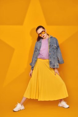 Modern gençlik görünüşü. Sarı arka planda parlak yaz kıyafetleri içinde bir yıldızla poz veren güzel bir genç kız. Güzellik, moda.