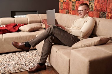 Zarif gündelik kıyafetler ve gözlüklü orta yaşlı iş adamı evde dizüstü bilgisayar ve gülümsemeyle çalışıyor. Başarılı yönetici kavramı.