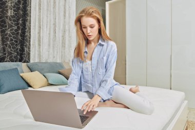 Güzel genç bir kadın rahat yatak odasında yatağında dizüstü bilgisayar kullanıyor. Yaşam tarzı. Evin içi, mobilyalar..