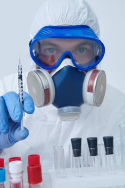 COVID-19. Doktor, mikrobiyolog, koruyucu kıyafetli bilim adamı laboratuarda aşılı bir şırınga tutuyor. Coronavirus testi.