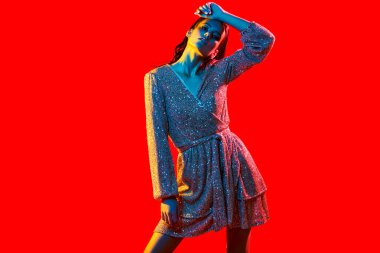 Makyaj ve makyaj malzemeleri. Kırmızı arka planda kırmızı, mavi ve sarı renkli bir ışıkta altın makyajlı muhteşem bir genç kadının portresi. Parti tarzı. Boşluğu kopyala.