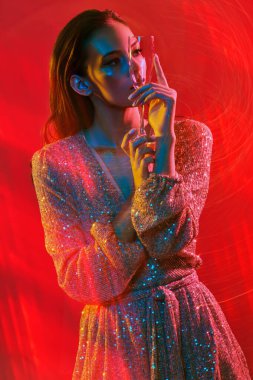 Makyaj ve makyaj malzemeleri. Renkli kırmızı, mavi ve sarı ışıkta elinde şampanya bardağıyla poz veren altın makyajlı genç bir kadının portresi. Parti biçimi. 