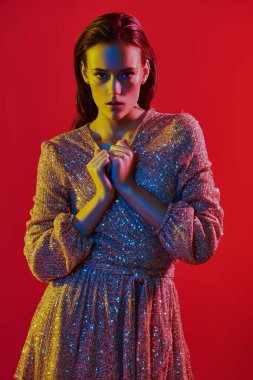 Makyaj ve makyaj malzemeleri. Kırmızı arka planda kırmızı, mavi ve sarı renkli bir ışıkta altın makyajlı muhteşem bir genç kadının portresi. Parti tarzı. Boşluğu kopyala.