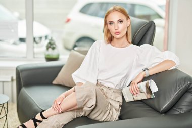 Zarif bir iş tarzı. Güzel genç bir kadın modern bir iç mekanda deri bir koltukta oturuyor. Mobilya ve iç dekorasyon.