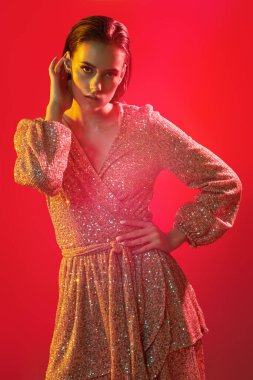 Makyaj ve makyaj malzemeleri. Kırmızı arka planda kırmızı, kırmızı ve sarı renkli bir ışıkta altın makyajlı muhteşem bir genç kadının portresi. Parti tarzı. Boşluğu kopyala.