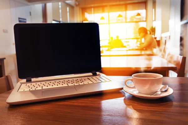 Xícara branca de café quente com laptop na mesa de madeira no café . — Fotografia de Stock