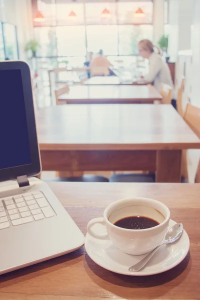 Weiße Tasse heißen Kaffee mit Laptop auf Holztisch im Café. — Stockfoto