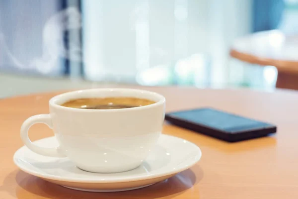 Weiße Tasse Kaffee mit Smartphone auf Holztisch. — Stockfoto