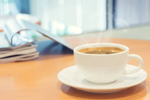 Bílý šálek kávy s časopisem na dřevo stůl. — Stock fotografie