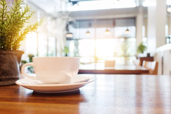 Šálek kávy s kouře na dřevěný stůl v café. — Stock fotografie