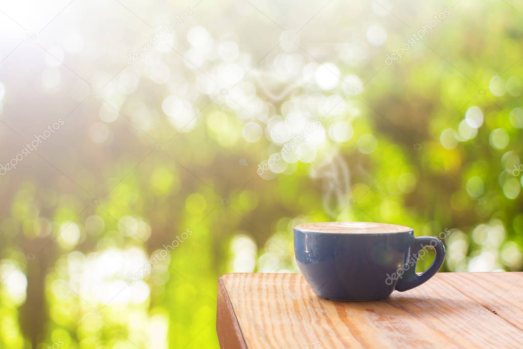Coffee cup with stream of vapour on wood table against natural b