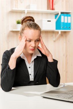 Business woman with a headache looking at the laptop in the offi clipart