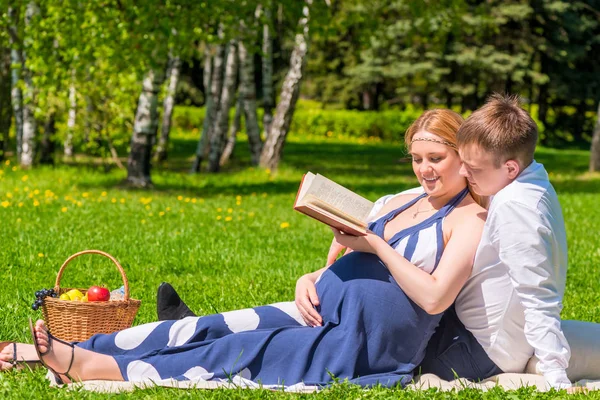 Mladí těhotná pár v parku, čtení knihy o těhotenství — Stock fotografie