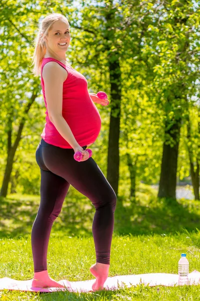 Mujer embarazada sonriente con mancuernas dedicadas a los deportes en el s — Foto de Stock