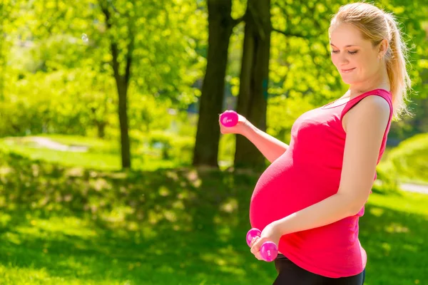 ピンクのシャツをダンベルで運動を行うことで妊娠中の女性 — ストック写真