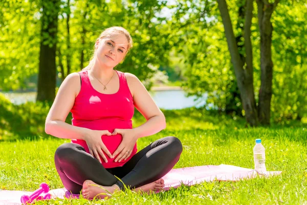 Vacker gravid kvinna visar hjärtat symbol händerna nära abd — Stockfoto