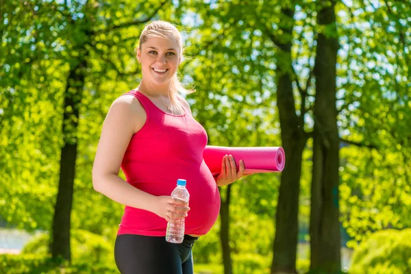 Lycklig kvinna med en matta och en flaska vatten efter ett träningspass — Stockfoto