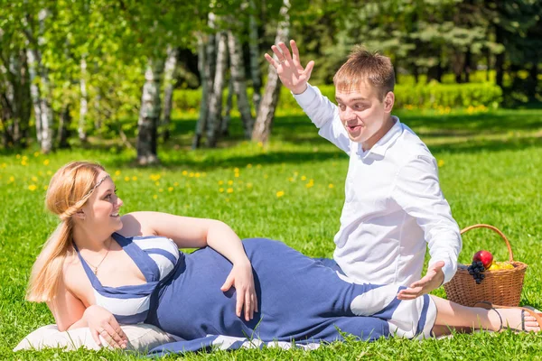 Mann erzählt seiner schwangeren Frau eine lustige Geschichte bei einem Picknick — Stockfoto