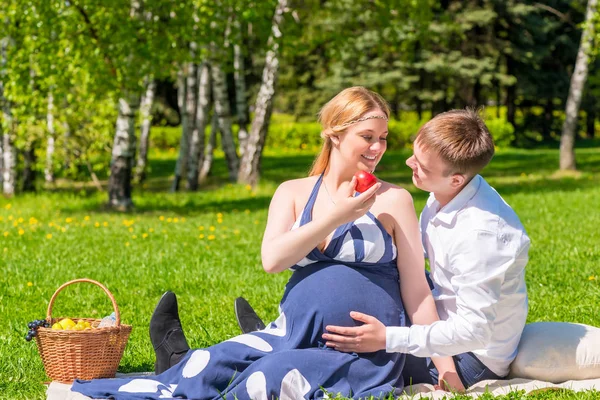 Joven pareja teniendo un picnic en un parque de la ciudad, una mujer es expecttin — Foto de Stock