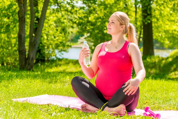 Mujer embarazada segura después de un entrenamiento con una botella de minera — Foto de Stock