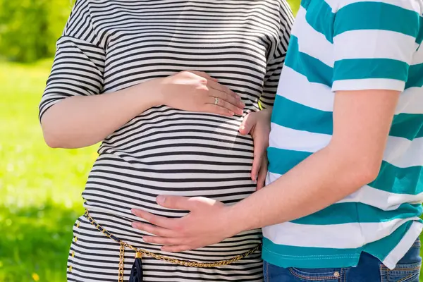 Futurs parents mains caressant ventre tourné dans un parc gros plan — Photo