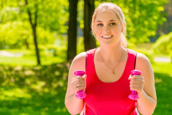 Mujer joven activa con mancuerna rosa haciendo ejercicio en el parque —  Fotos de Stock