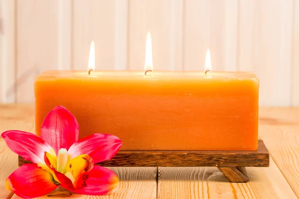 Grande bougie allumée et fleur tropicale sur une table en bois — Photo